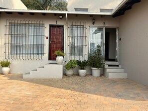 A building with two numbered doors, a red door, and a white door with a window. There are potted plants on the steps and a brick-paved area in front. - Menlyn Stay (Pretoria)