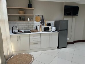 A modern kitchen with white cabinets, a microwave, a refrigerator, and a flat-screen TV mounted above the counter. - Menlyn Stay (Pretoria)