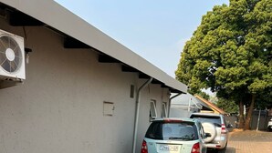 A parking area with a paved surface, a white wall, and a tree. - Menlyn Stay (Pretoria)
