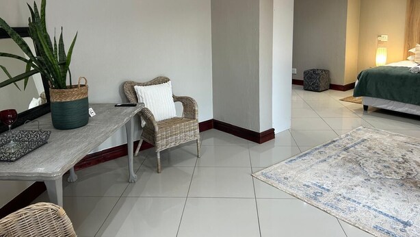 A hotel room with a bed, a sitting area with a chair and table, a potted plant, and a rug. - Menlyn Stay (Pretoria)