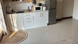 A modern kitchen with white cabinets, a microwave, a coffee maker, and a refrigerator. - Menlyn Stay (Pretoria)