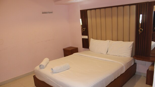 Una habitación de hotel con una cama grande, un cabecero de madera, una mesita de noche y una lámpara fijada a la pared.