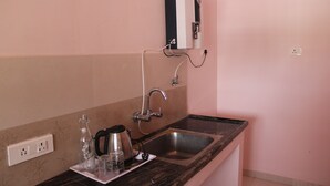 Una cocina con un lavamanos, una cafetera, un hervidor y un dispensador de agua en la pared.