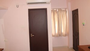 Una habitación con puerta cerrada, un equipo de aire acondicionado en la pared, una cortina y un ventanal pequeño.