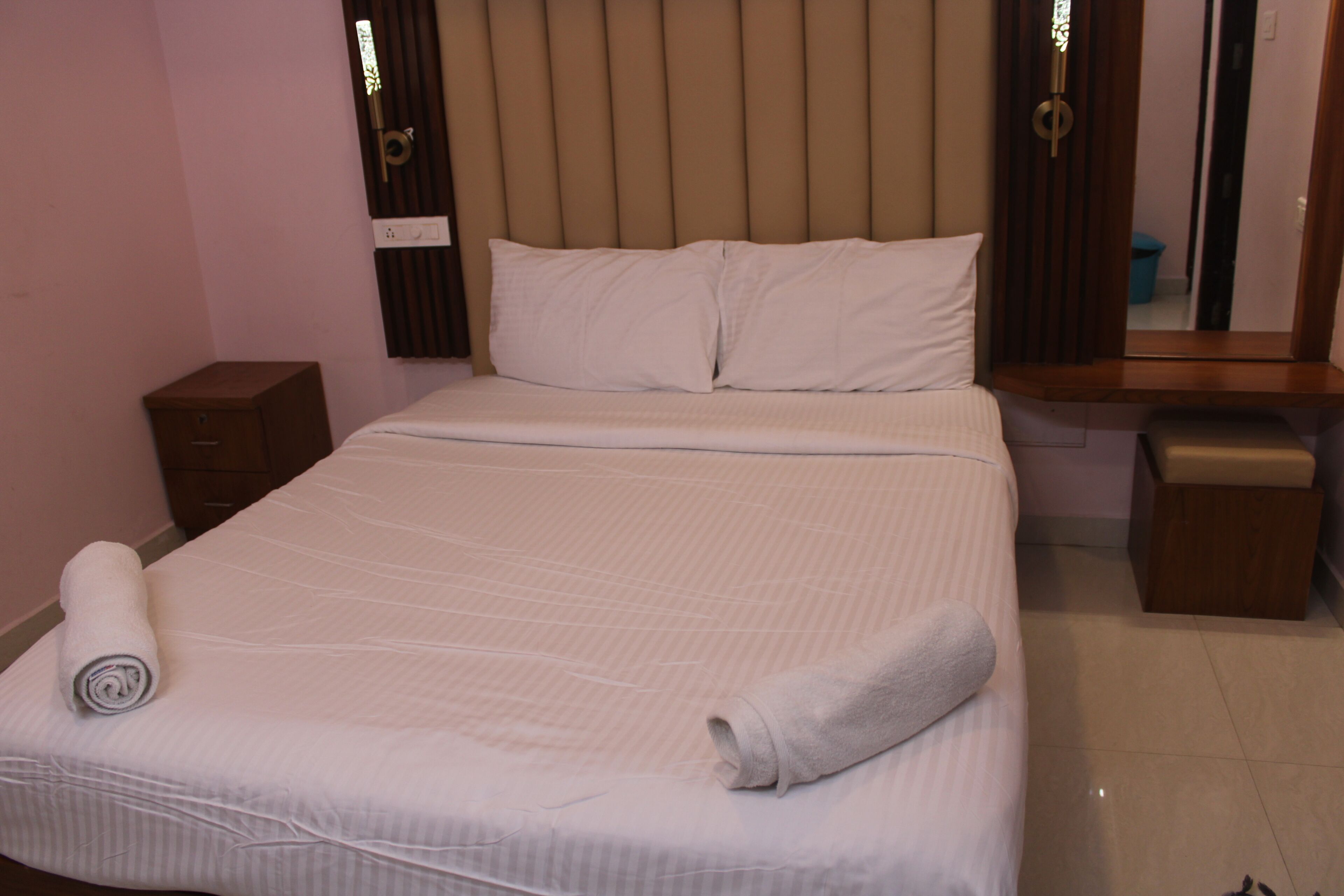 A neatly made bed with a rolled towel, a bedside table, and a nightstand.
