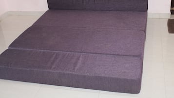 A single bed with a mattress and a headboard in a room with white tiled flooring.