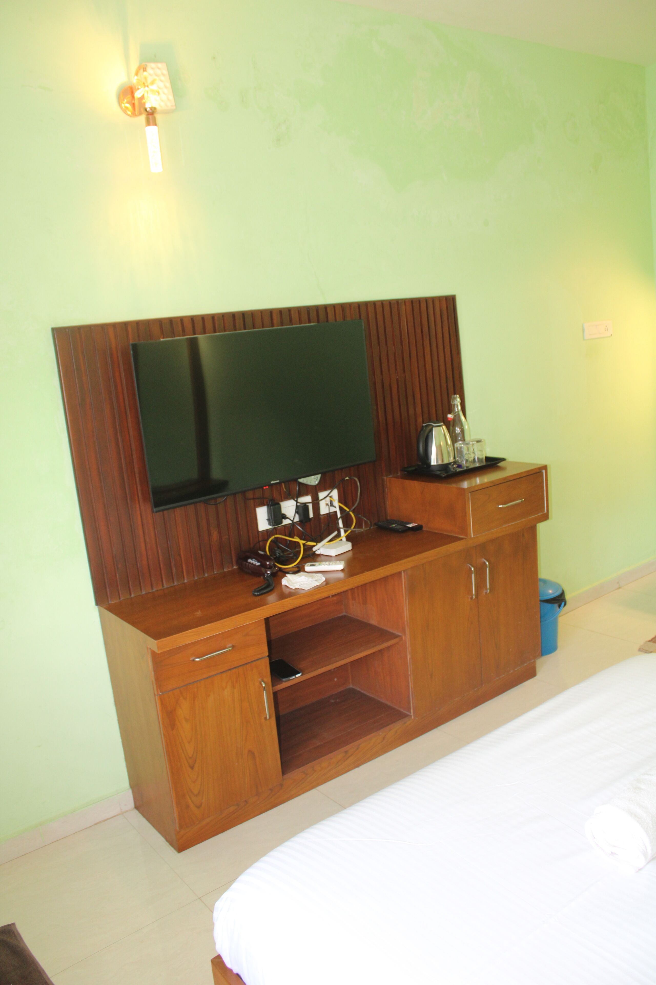 A bedroom with a bed, a wooden dresser with a flat-screen TV, and a desk with various items.