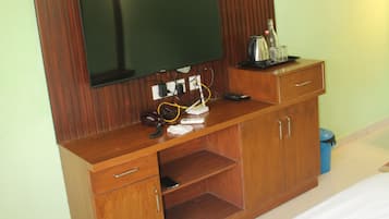 A bedroom with a bed, a wooden dresser with a flat-screen TV, and a desk with various items.