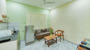 A compact living space with a kitchenette, a refrigerator, a sofa, a dining table, and a ceiling fan.