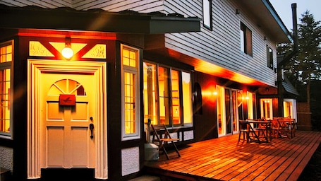 A wooden deck with outdoor seating and a lit entrance door.