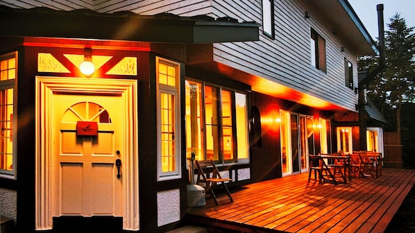 A wooden deck with outdoor seating and a lit entrance door.