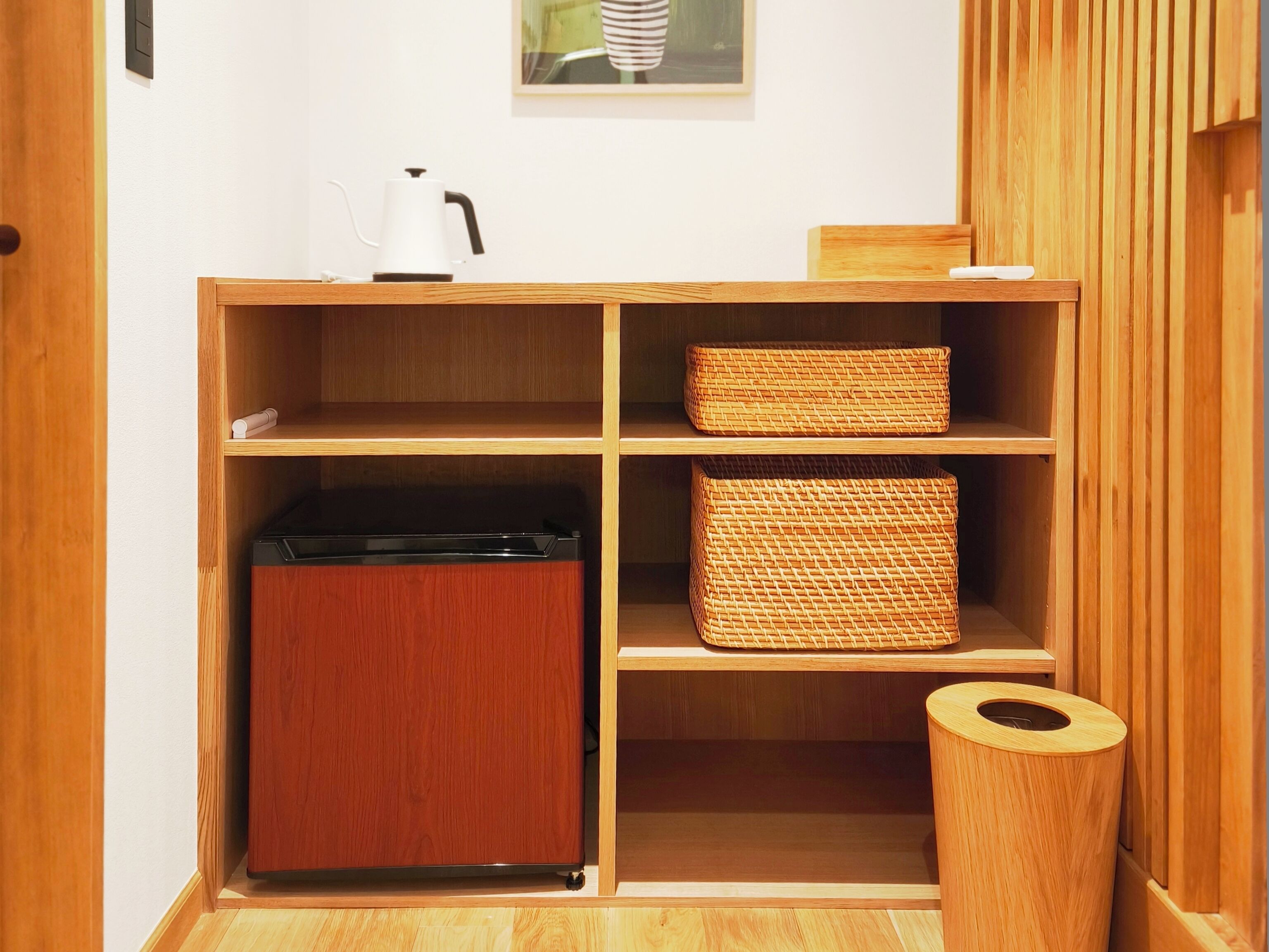 A wooden cabinet with open shelves, a small appliance, and a trash bin.
