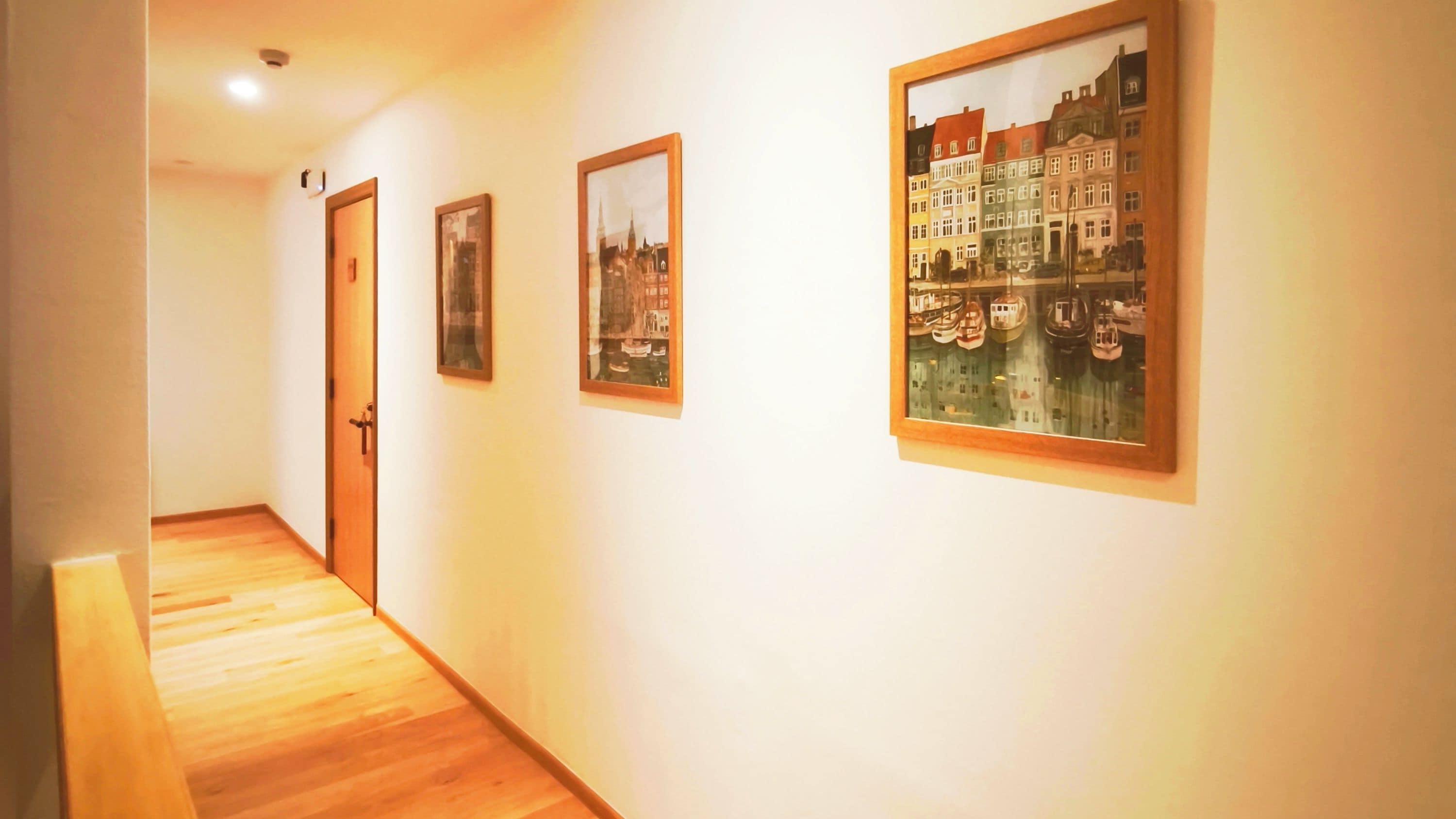 A hallway with wooden flooring, a door, and three framed pictures on the wall.