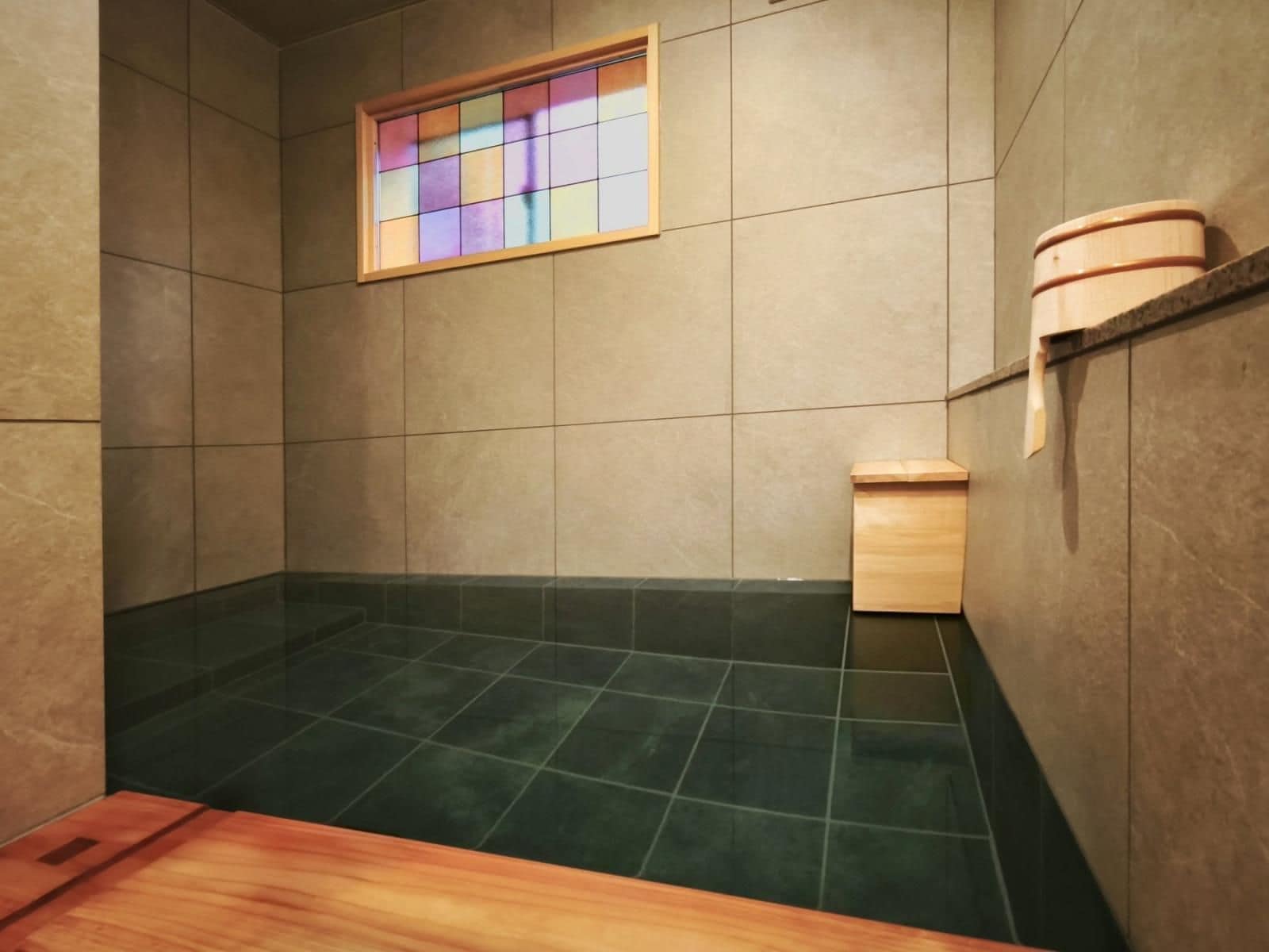 A small, tiled bathroom with a wooden bench, a wooden cabinet, and a stained glass window.