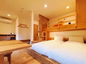 Una habitación con una cama litera, un escritorio de madera, un perchero y una pequeña zona de kitchenette.