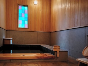 Un intérieur en bois, avec un sol carrelé en pierre, un banc en bois et un petit tabouret en bois.