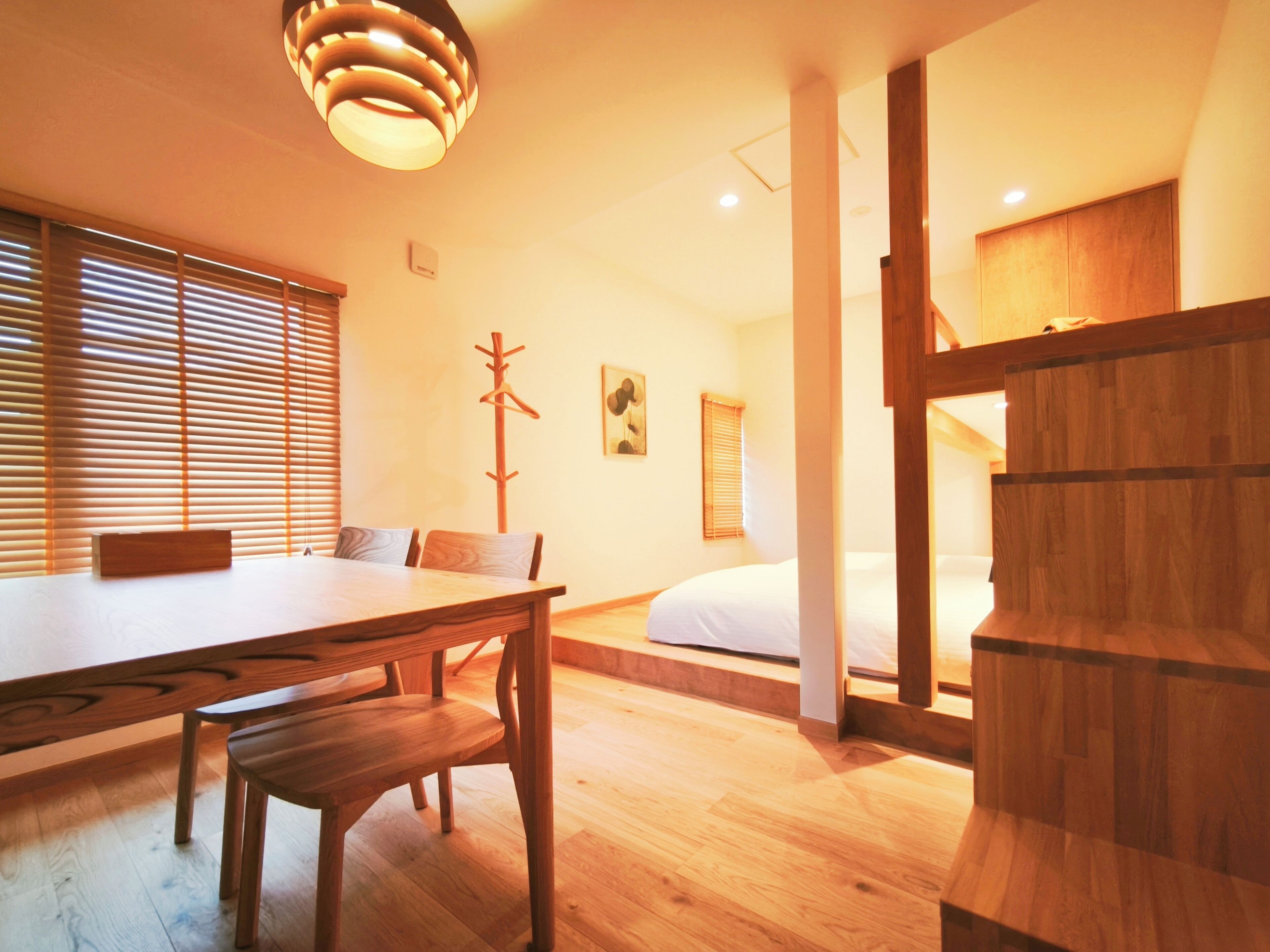 A room with a wooden dining table, chairs, a coat rack, a bed, and a wooden cabinet.