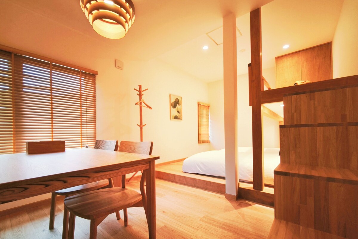 Una habitación con una mesa de comedor de madera, sillas, perchero, cama y un armario de madera.