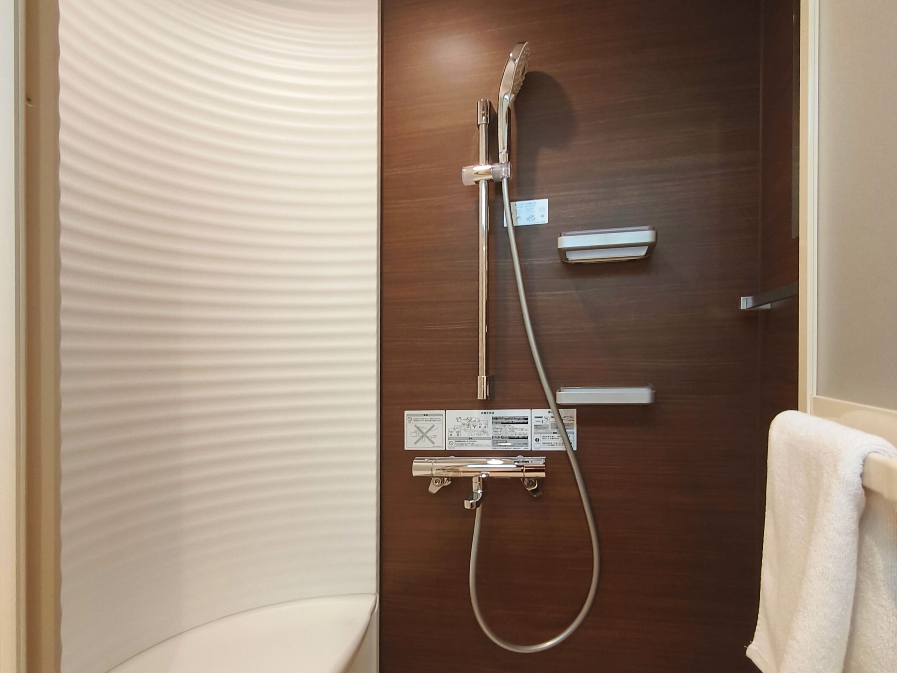 A bathroom with a wooden door, a shower with a handheld showerhead, and a towel rack.