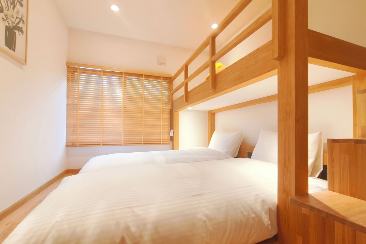 Une chambre avec un lit superposé, une tête de lit en bois et une fenêtre avec des stores.
