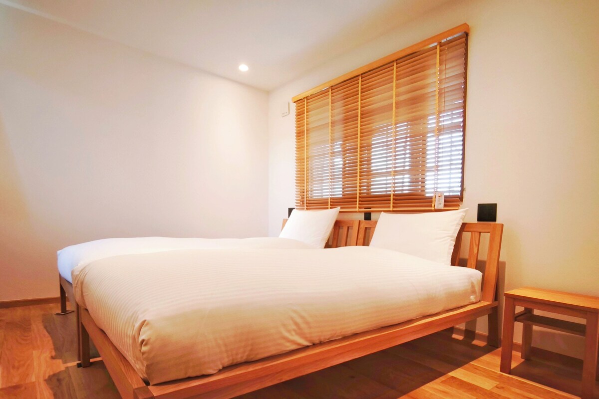 A bedroom with a wooden bed, a nightstand, and a window with blinds.