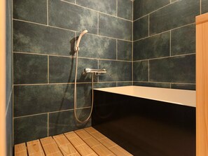 Un baño con paredes de azulejos oscuros, suelo de madera y una bañera blanca.