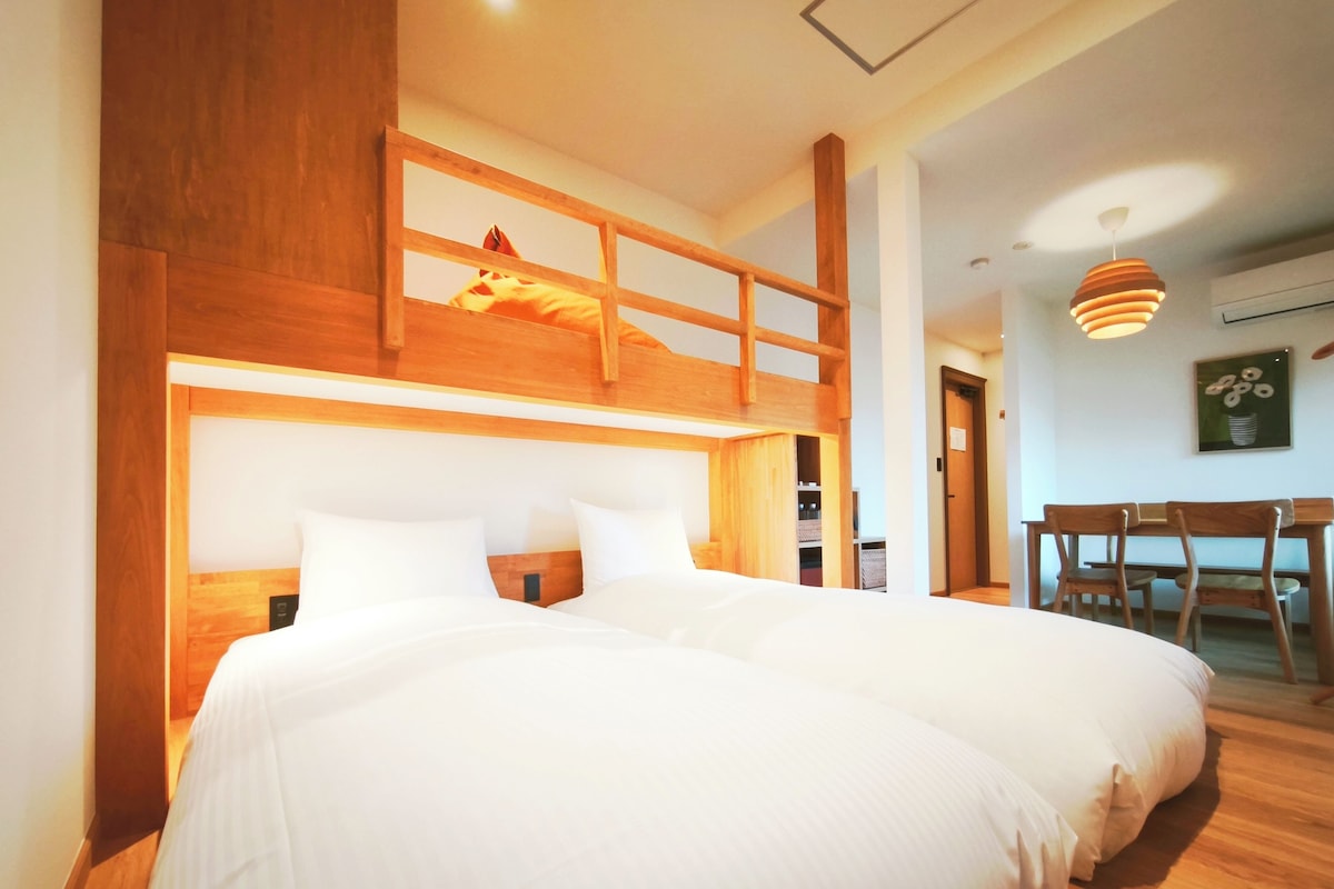 Une chambre avec deux lits, un lit superposé en bois, un bureau et une chaise.