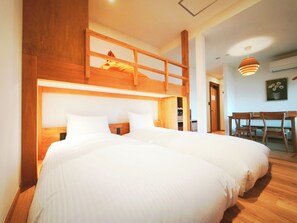 Une chambre avec deux lits, un lit superposé en bois, un bureau et une chaise.