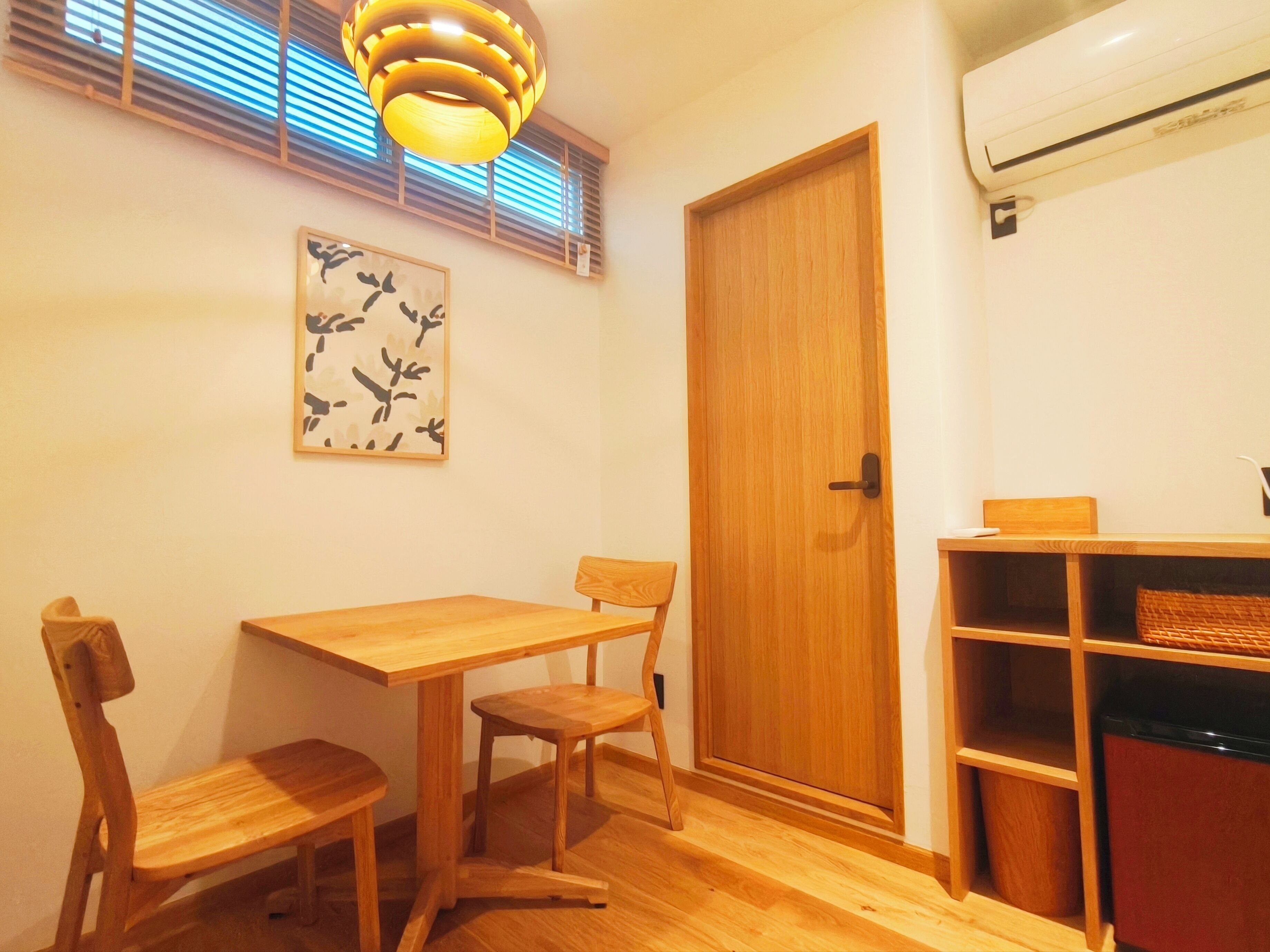 A room with a wooden dining table and chairs, a wooden door, and a wall-mounted air conditioner.