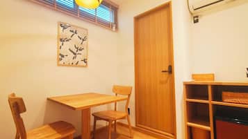 A room with a wooden dining table and chairs, a wooden door, and a wall-mounted air conditioner.