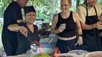 A group of people cooking outdoors with a grill and a large green fruit.