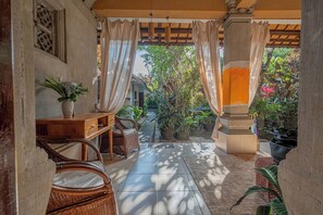 A covered outdoor seating area with wicker furniture, a potted plant, and a view of a garden. - Pondok Alami Villas 5BR & Pool (Ubud)