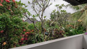 Un balcón con vistas a un jardín exuberante, una casa con techo de tejas y una palmera.