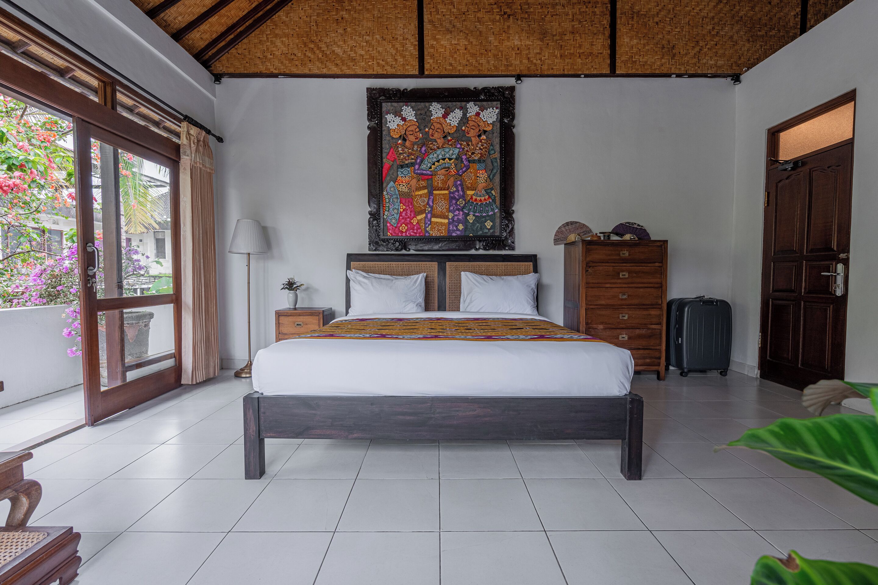 A bedroom with a large bed, a wooden headboard, a nightstand, a dresser, and a window with curtains.