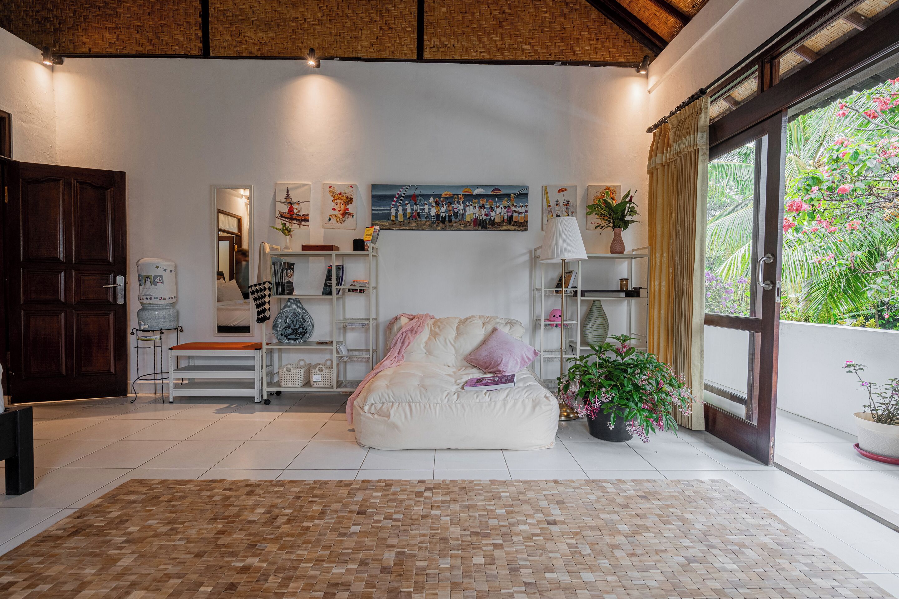 A spacious living area with a large window, a white sofa, and a bookshelf.