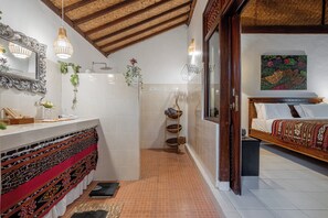 Baño con ducha, lavamanos y espejo. Hay plantas y un perchero para toallas.