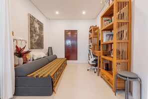 A modern living room with a sofa, a bookshelf, a painting, and a door. - Pondok Alami Villas 5BR & Pool (Ubud)
