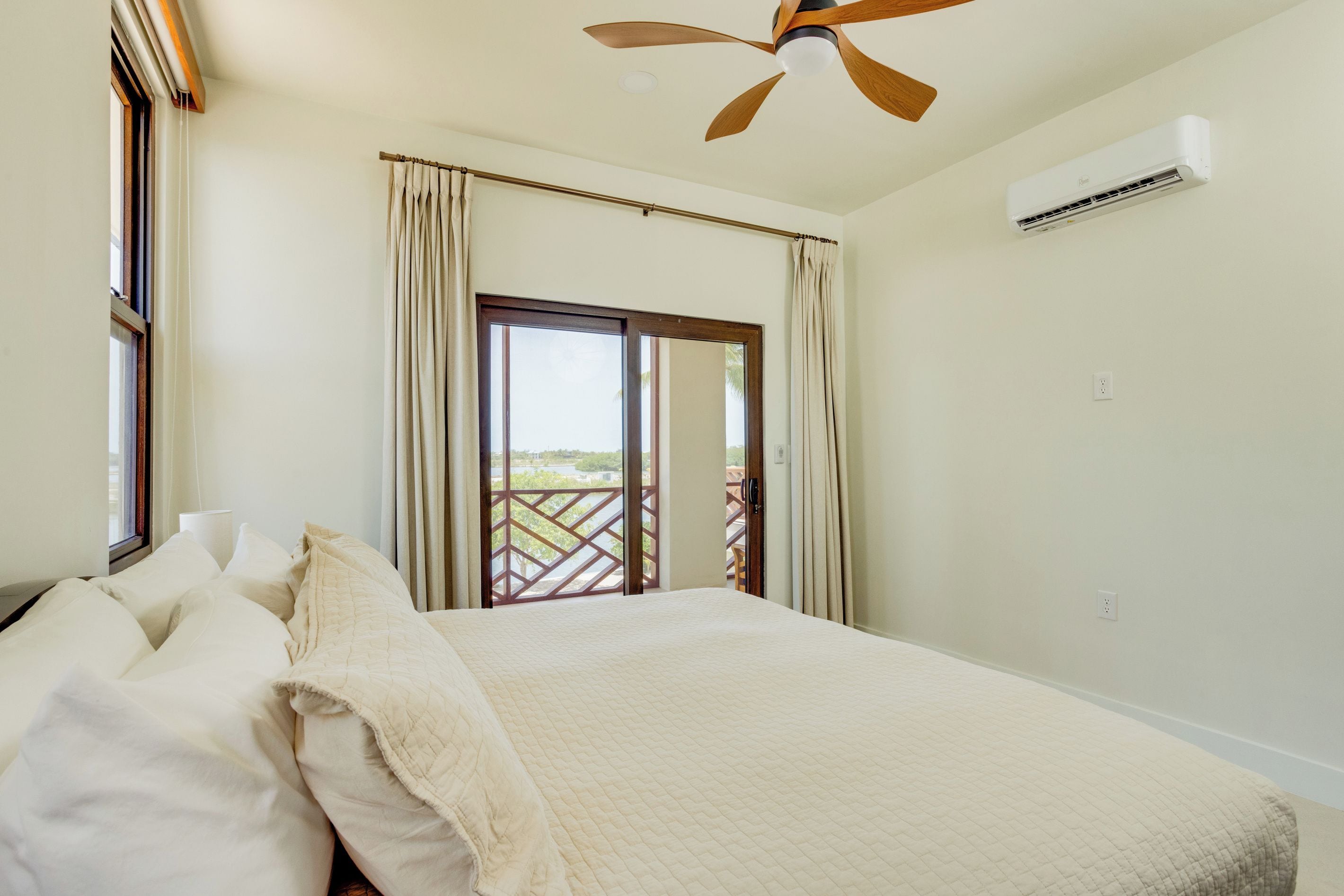 Ein Schlafzimmer mit einem Bett, einem Deckenventilator, einer Klimaanlage und Blick durch ein Fenster.