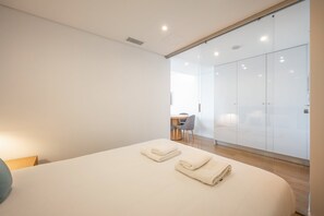 Un dormitorio moderno con una cama grande, un escritorio y un muro divisorio de vidrio.