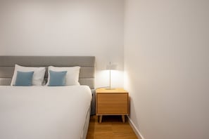 A neatly made bed with two pillows, a bedside table with a lamp, and a wooden nightstand. - GuestReady - Solace Beach Sesimbra (Sesimbra)