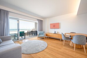 A modern hotel room with a balcony, a flat-screen TV, a dining area, and a seating area. - GuestReady - Solace Beach Sesimbra (Sesimbra)