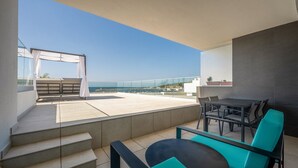 Un balcon avec une table et des chaises, une vue sur la mer et un escalier menant à un niveau supérieur.
