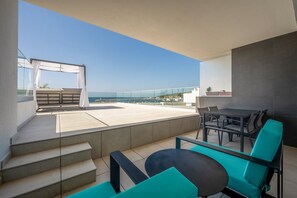 Ein Balkon mit Tisch und Stühlen, Blick aufs Meer und eine Treppe zu einer oberen Ebene.