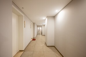 Ein langer, schmaler Hotelkorridor mit Türen auf der linken Seite, einem roten Teppich und einem gefliesten Boden.
