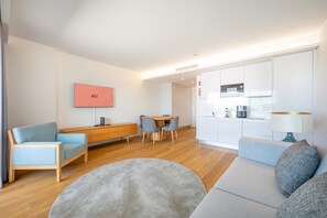 Un salon moderne avec un canapé, un tapis rond, un téléviseur et un coin repas avec des chaises.