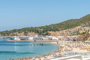 A coastal town with a beach, boats, and a hilly backdrop. - GuestReady - Solace Beach Sesimbra (Sesimbra)