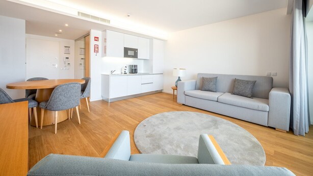 Un salon moderne avec un canapé gris, une table basse ronde et un coin repas comprenant une table en bois et des chaises grises.