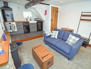 A modern kitchen with a built-in oven, a sink, and a stove. There is a blue sofa with plaid cushions in the living area, and a wooden chest of drawers. - 1 bedroom accommodation in Cockermouth (Cockermouth)