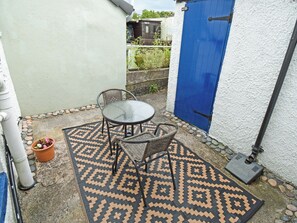 A patio with a glass table and wicker chairs, a patterned rug, and a blue door. - 1 bedroom accommodation in Cockermouth (Cockermouth)