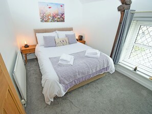 A neatly made bed with a striped blanket, a bedside lamp, and a floral pillow. - 1 bedroom accommodation in Cockermouth (Cockermouth)